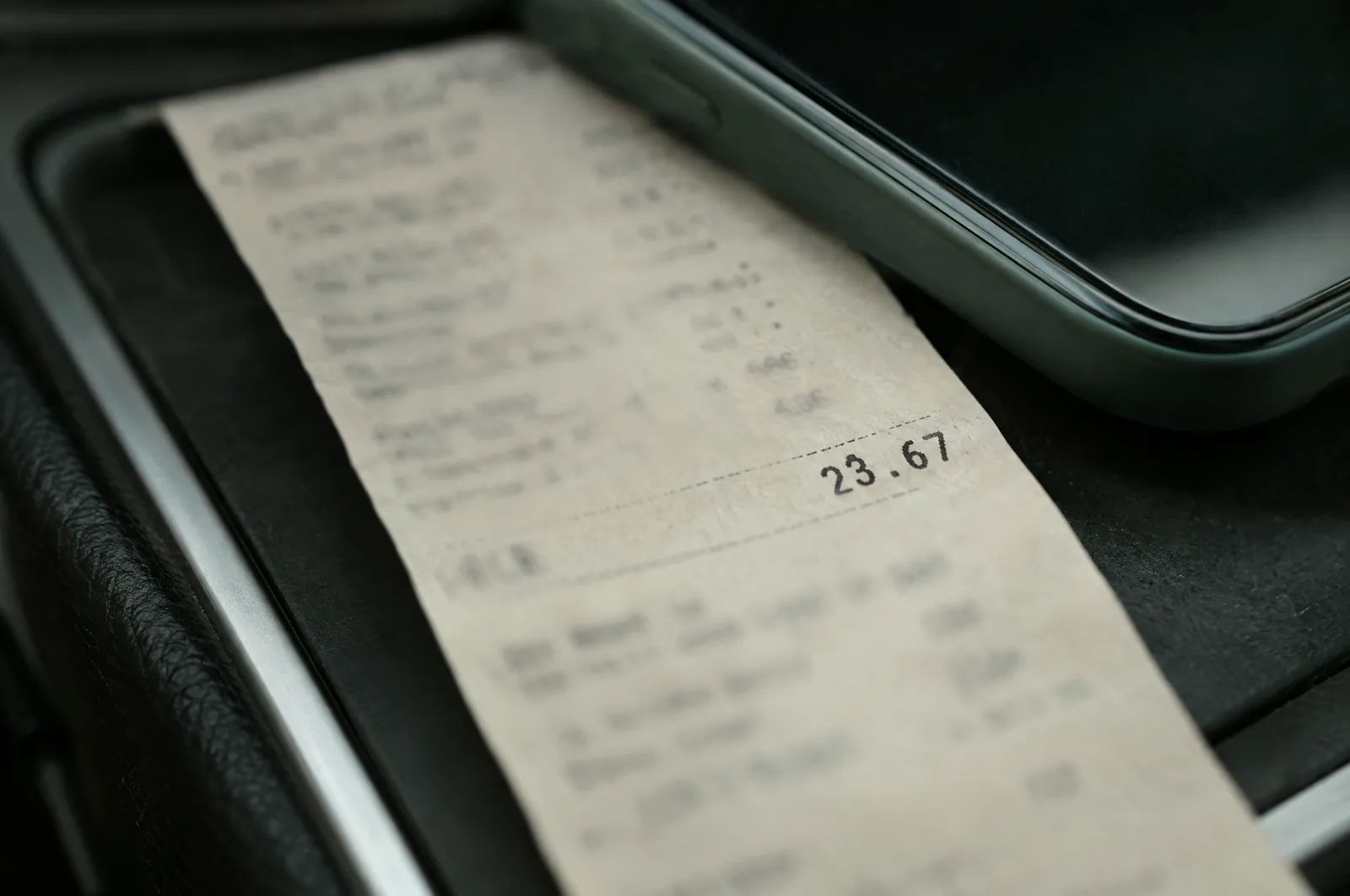 The itemized lines of a pharmacy receipt on a car console, photographed close, with the edge of a phone resting over its top.